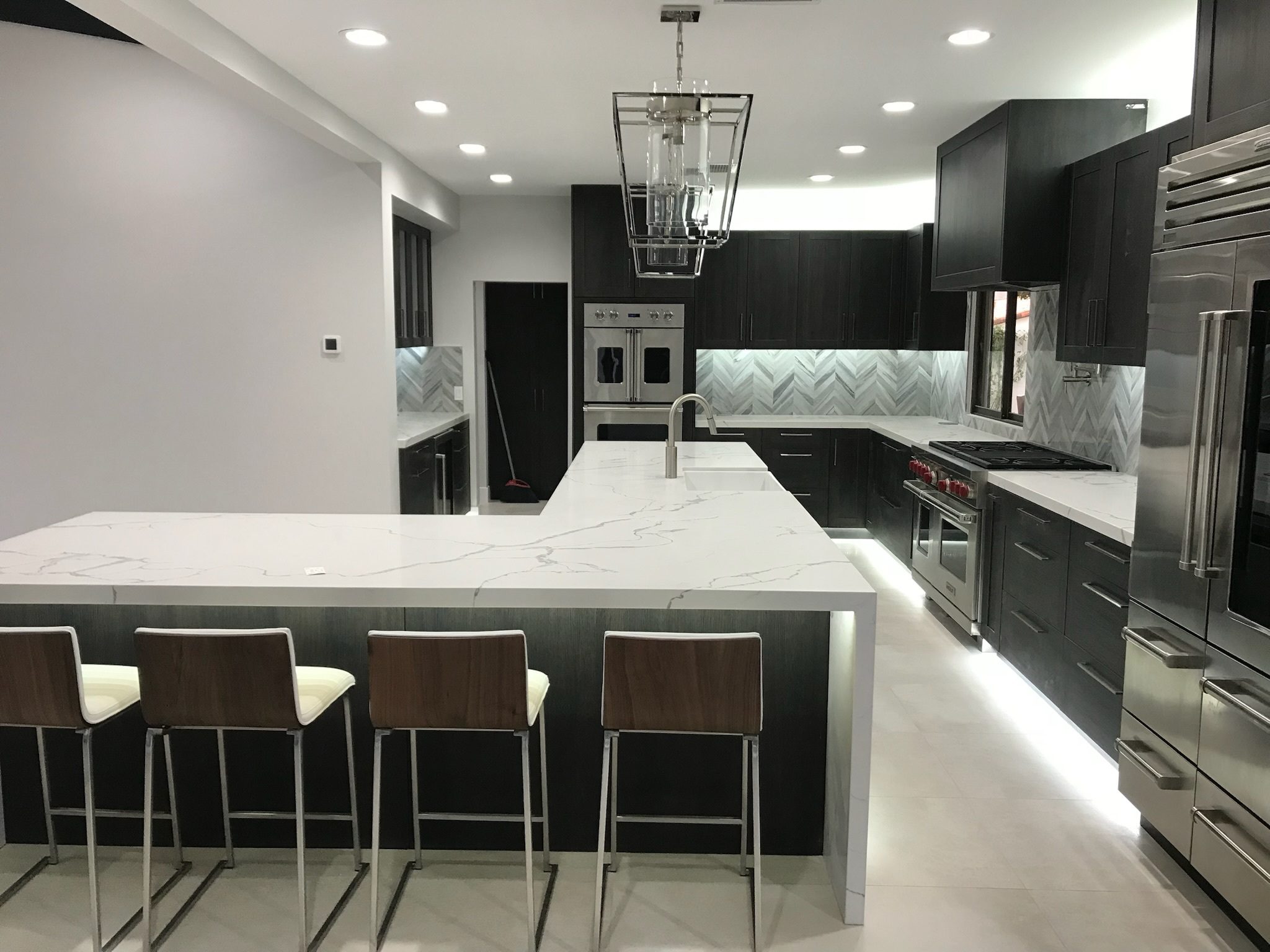 Bullet Image Modern kitchen interior featuring dark wood cabinets, white marble countertops, stainless steel appliances, and a central island with bar stools.